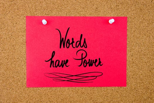 Red paper note with handwritten text Words Have Power pinned on cork board with white thumbtacks