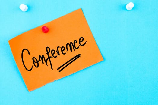 Conference written on orange paper note pinned on cork board with white thumbtack, copy space available