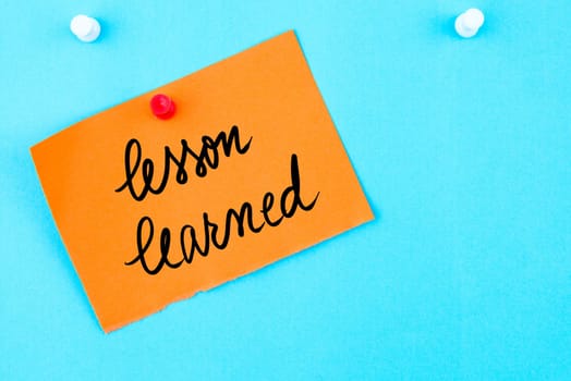 Lesson Learned written on orange paper note pinned on cork board with white thumbtack, copy space available