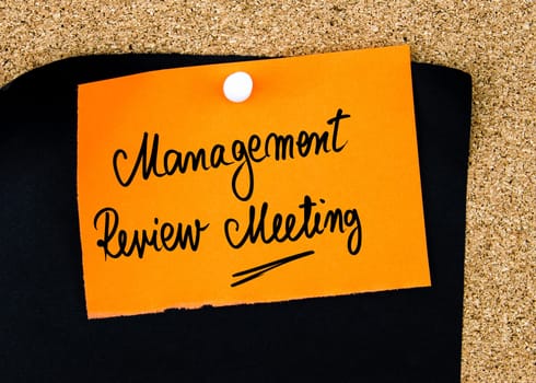 Management Review Meeting written on orange paper note pinned on cork board with white thumbtacks, copy space available