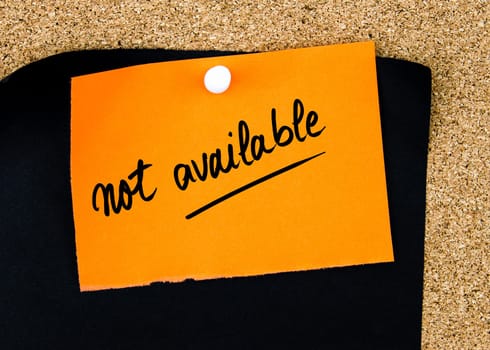 Not Available written on orange paper note pinned on cork board with white thumbtacks, copy space available