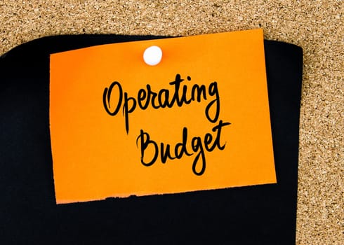 Operating Budget written on orange paper note pinned on cork board with white thumbtacks, copy space available