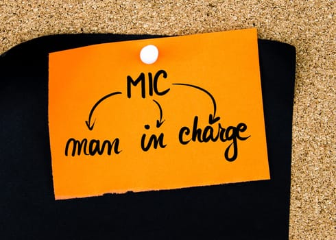 Business Acronym MIC as Man In Charge written on orange paper note pinned on cork board with white thumbtacks, copy space available