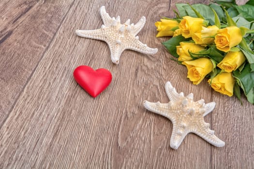 White starfishes, heart and yellow roses on a wooden background