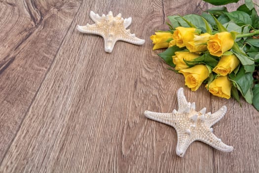 White starfishes and yellow roses on a wooden background
