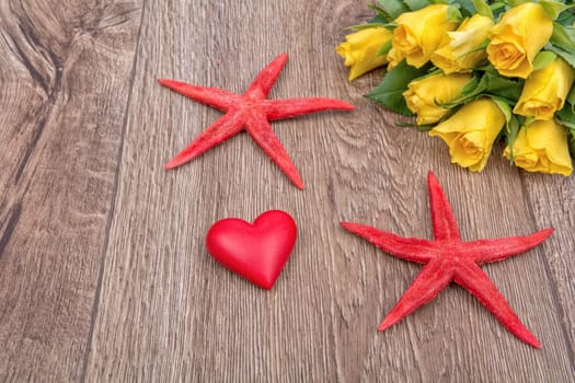 Red starfishes, heart and yellow roses on a wooden background