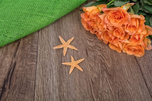 Orange starfishes and orange roses on a wooden background
