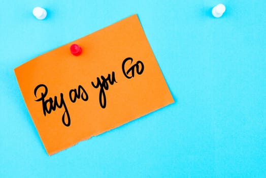 Pay As You Go written on orange paper note pinned on cork board with white thumbtack, copy space available