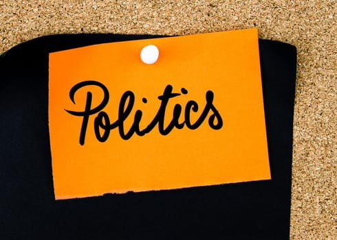 Politics written on orange paper note pinned on cork board with white thumbtacks, copy space available