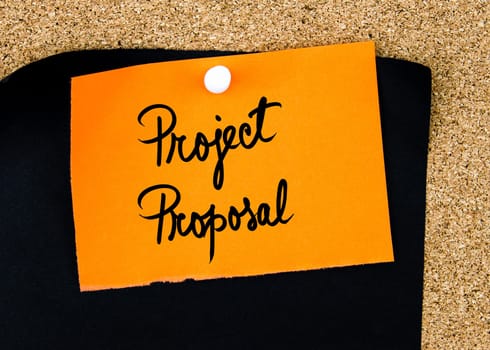 Project Proposal written on orange paper note pinned on cork board with white thumbtacks, copy space available