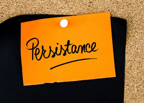 Persistance  written on orange paper note pinned on cork board with white thumbtacks, copy space available