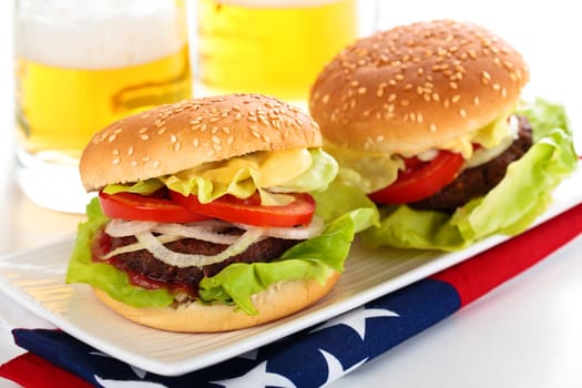 Beer and two tasty hamburgers on white table.
