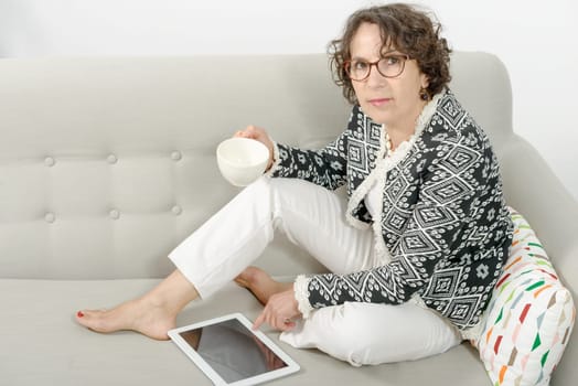 mature woman with tablet, drinking tea on the sofa