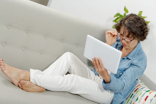 a beautiful mature woman with a tablet on the couch