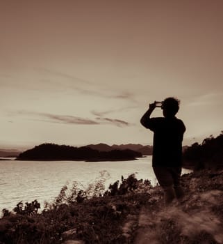 Beautiful nature landscape of mountain with lake, silhouette man take photo with smart phone. Vintage color style