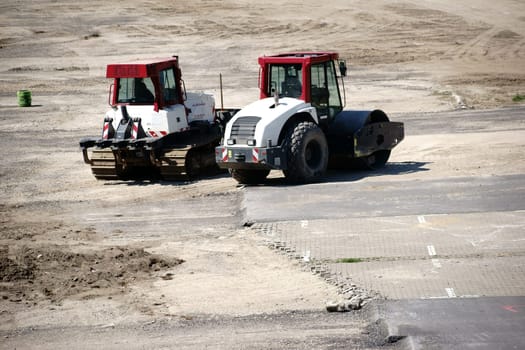 A roller and a bulldozer stand on a free area of a construction site.