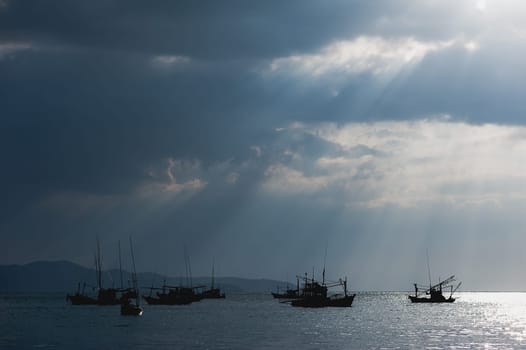 Scenery of fishing boats and yachts with sunlight shining through cloudy sky and reflections of golden clouds on smooth water, in Thailand