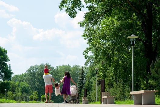 Happy family of four people walking on the city park in the summer sunny day