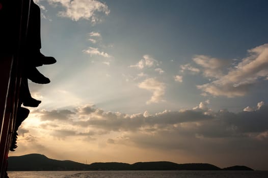 People sit on the ferry, his legs dangling over the sea. sunset, clouds, people go to work