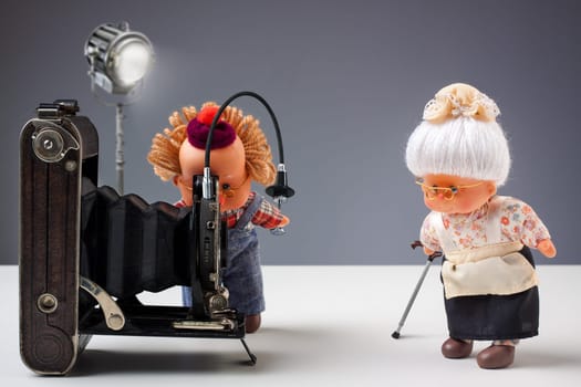 Puppets of senior photographer taking pictures of his old ladies with vintage camera in studio
