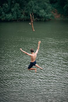 a young man jumping with a rope into the river, outdoors