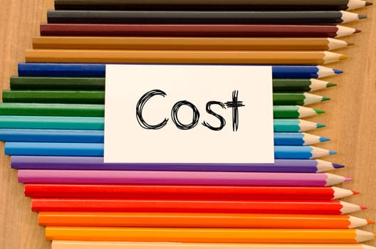 Cost text concept and colored pencil on wooden background