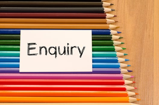 Enquiry text concept and colored pencil on wooden background