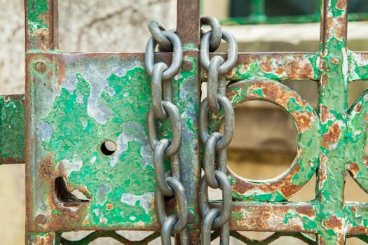 A green rusty lock on an iron door with a chain