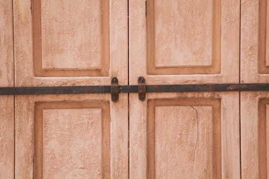 Rose weahtered wood door closed by a rusty rod