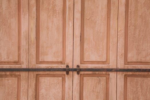 Rose weahtered wood door closed by a rusty rod