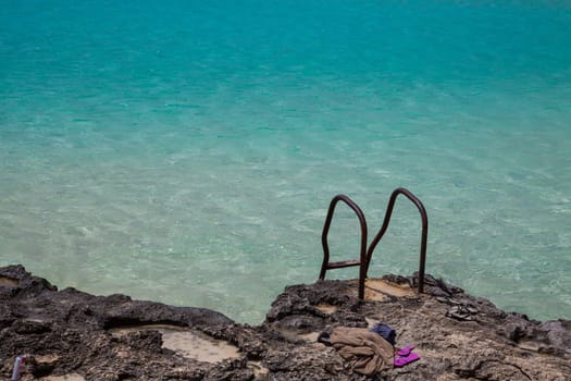 Rusty stairs on rocks to pool-like sea waters with flip-flop