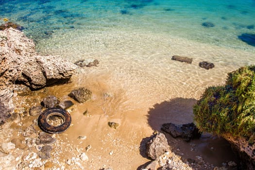 Wonderful sunny beach with blu water and used tire
