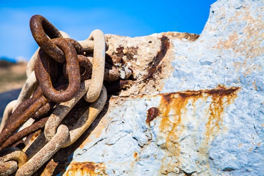 Rusty weathered chains hanged on sea rocks