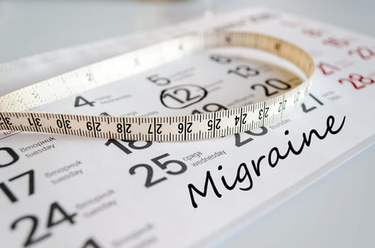 Migraine text concept over tape measure and calendar background..