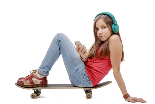 pretty young girl posing with a skateboard, sitting on skate, listen a music
