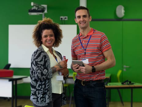 Two teachers standing together with paper work and a digital tablet. They are smiling and looking at the camera.