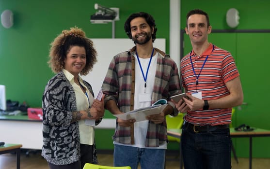 Three teachers standing together with paper work and a digital tablet. They are smiling and looking at the camera.