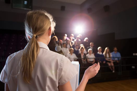 Female student making a speech. She is standing at a podium and smiling to the crowd.