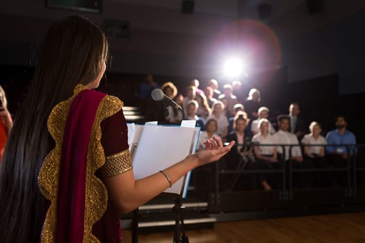 Female student making a speech. She is standing at a podium and talking to the crowd of people.