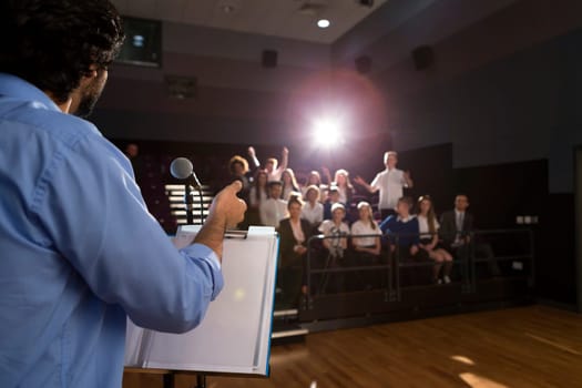 Male teacher giving a speech in a lecture hall to students and teachers.