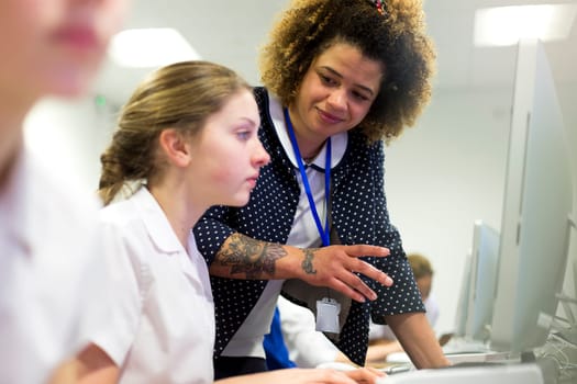 Female teacher with tattoos helping one of her students, who is doing work on a computer.