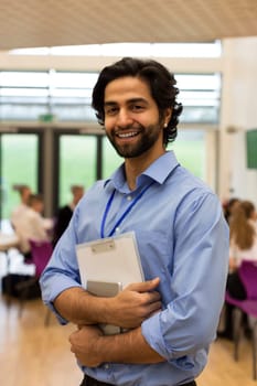 Waist up portrait of a school teacher. He is holding some paperwork and a digital tablet.