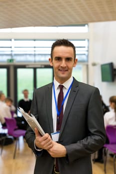 Waist up portrait of a school teacher. He is holding some paperwork and a digital tablet.