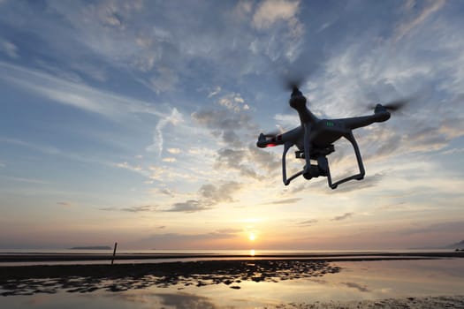 KAGAWA, JAPAN - JUNE 10, 2016: Remote controlled drone Dji Phantom 3 equipped with high resolution video camera flying above the beach against a sunset.