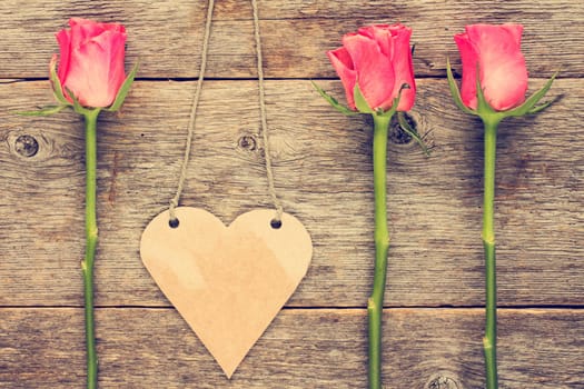 Blank heart shaped tag and roses on wooden background.