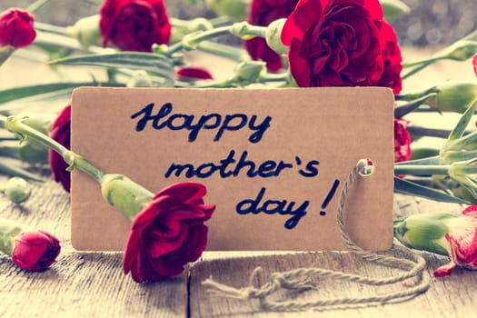 Mothers day card with carnations on wooden board. Vintage filter.