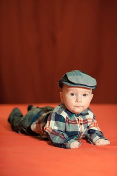 Cute baby in a tweed flat cap with a red background, the child&#39 s emotions