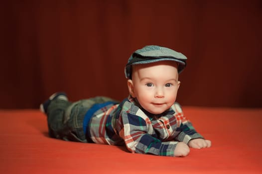 Cute baby in a tweed flat cap with a red background, the child&#39 s emotions