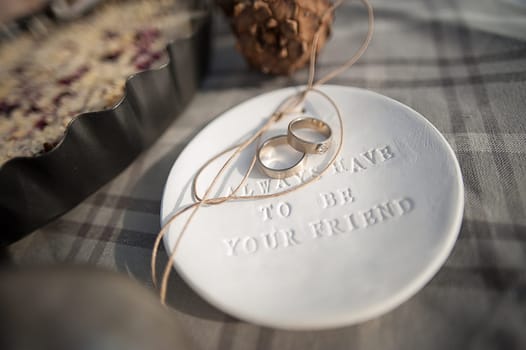 Wedding rings in white gold, white clay saucer with the word always have to be your friend