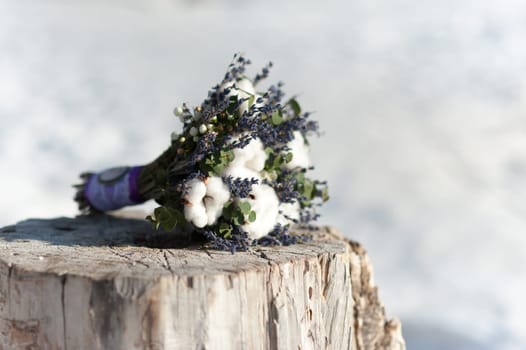 Beautiful wedding bridal bouquet lying on a tree stump made of cotton and blue colors, winter